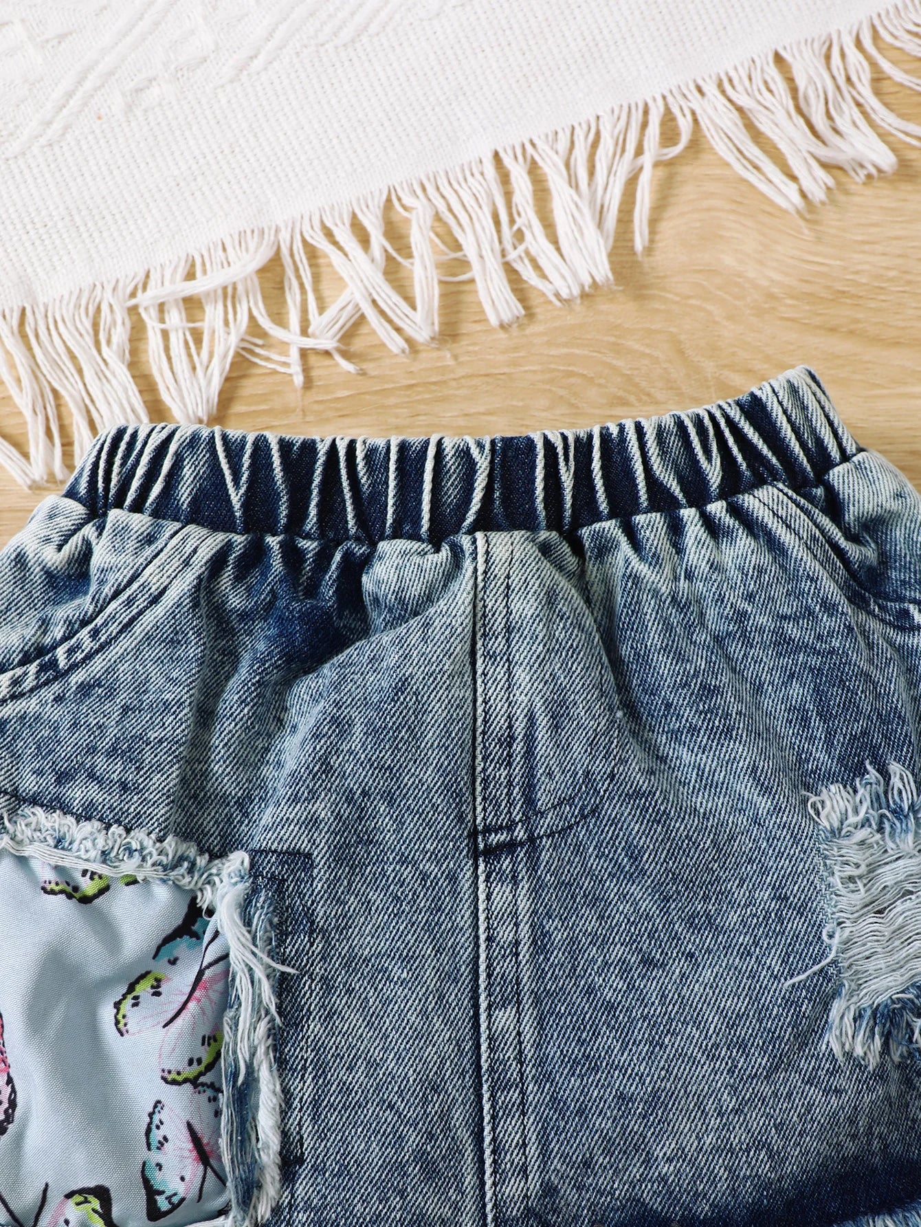 Close up highlighting the hem and stitching on the baby girls letter print romper and denim skirt set