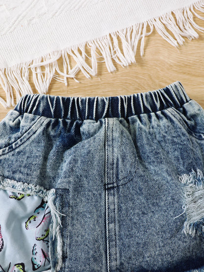 Close up highlighting the hem and stitching on the baby girls letter print romper and denim skirt set