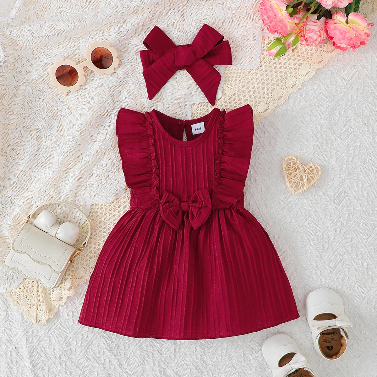 Baby girl wearing a solid colour sleeveless dress with ruffled edges and a headband
