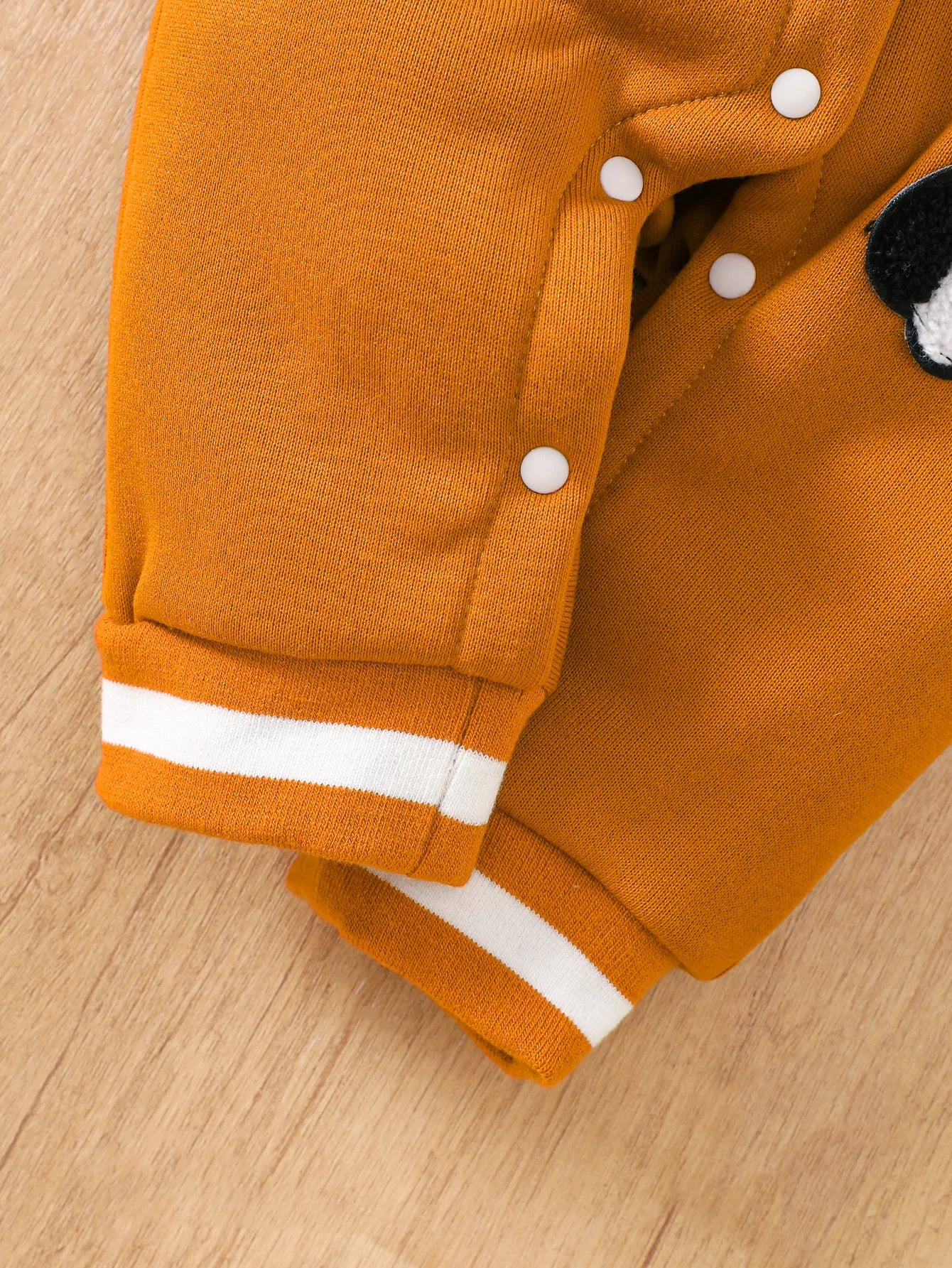 Baby boy wearing a caramel and orange fleece-lined baseball style romper