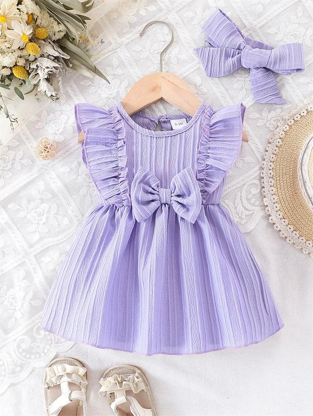 Baby girl wearing a purple ruffle dress with a bow and matching headband